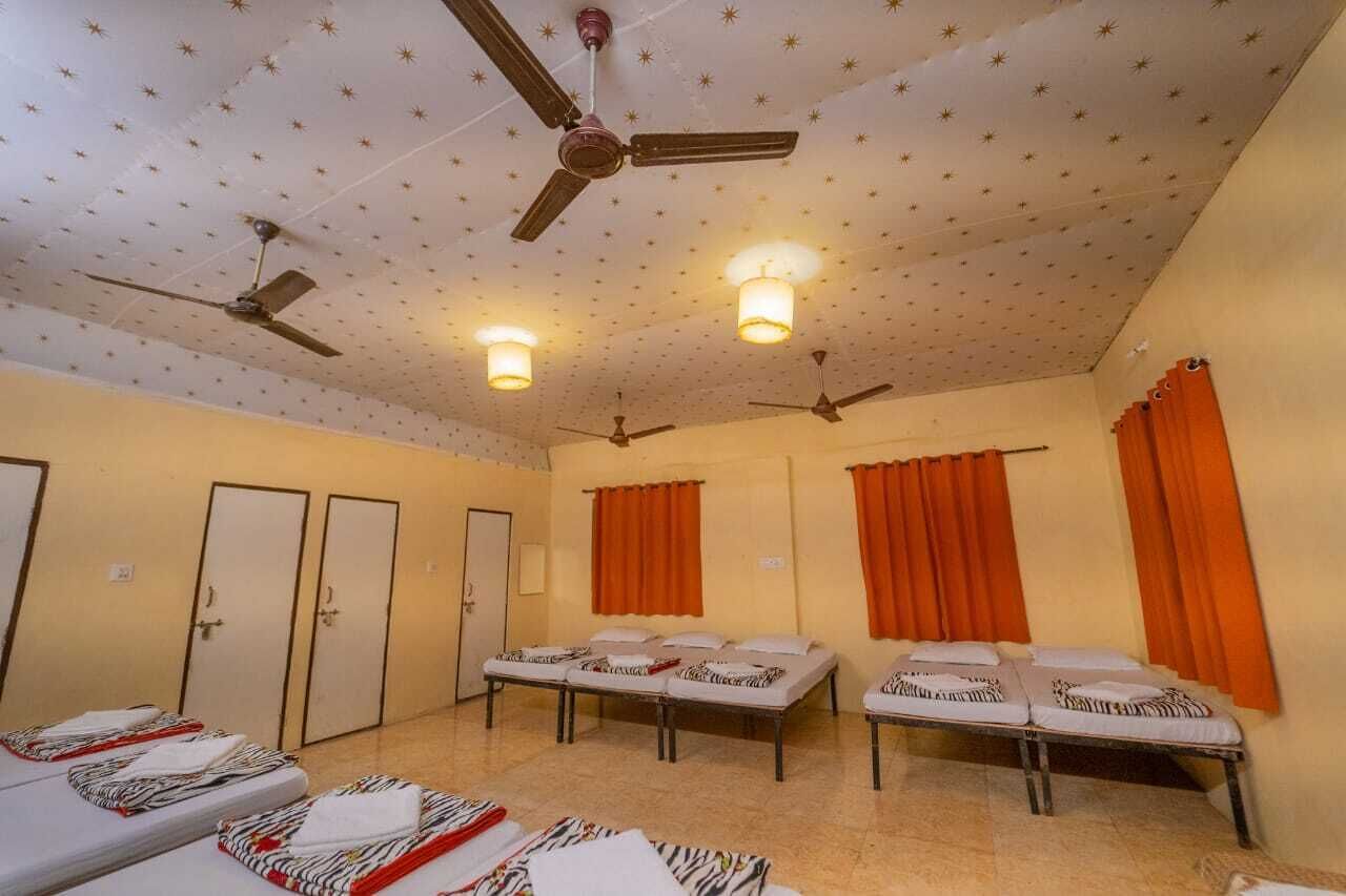 A room with four beds, two ceiling fans, and orange curtains.