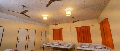Una habitación con cuatro camas, dos ventiladores de techo y cortinas color naranja.