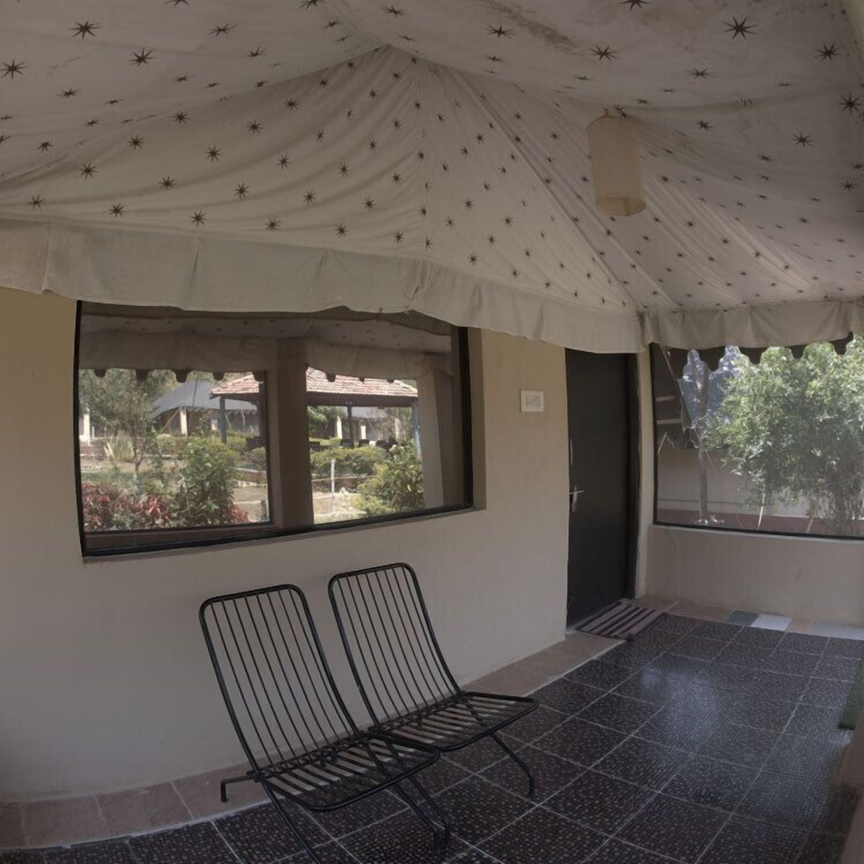 A covered outdoor seating area with two metal chairs, a large window, and a tiled floor.