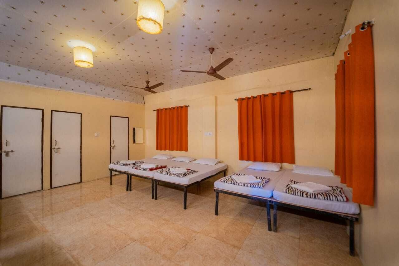 Une chambre d’hôtel avec deux lits simples, un ventilateur de plafond et des rideaux orange.