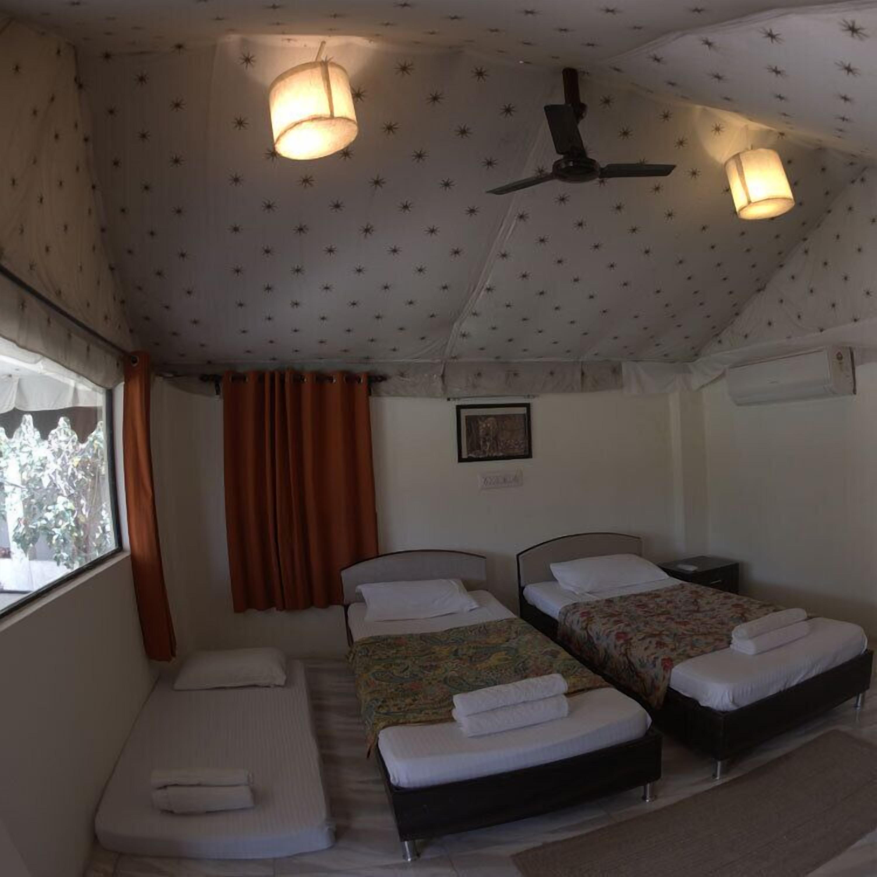 A room with two single beds, a window with curtains, a ceiling fan, and a wall-mounted air conditioning unit.