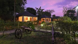 Un edificio de estilo tradicional con tejado de paja, rodeado de abundante vegetación y un carro rústico en primer plano.