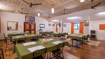 A conference room with multiple tables, chairs, ceiling fans, and a television screen.