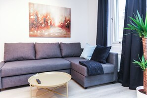 Un salon moderne avec un canapé d’angle gris, une table basse ronde, un tableau au mur et une plante en pot.