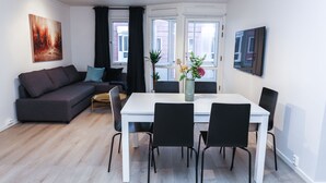 Un moderno salón con un sofá, una mesa de comedor con sillas, un florero con flores y un cuadro en la pared.