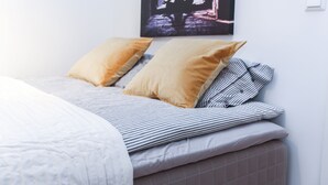 Una cama bien hecha con ropa de cama a rayas y dos almohadas, un cuadro en la pared y un interruptor de luz.