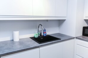 Une cuisine moderne avec un évier noir, des armoires blanches et un plan de travail gris.