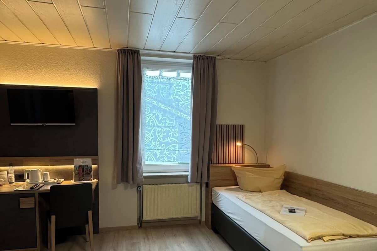 Hotellihuone, jossa on sänky, työpöytä, televisio ja ikkuna, jossa on verhot.