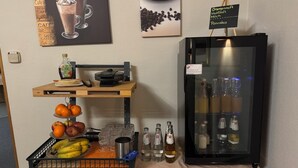 Una estación de bebidas con una máquina de café, un refrigerador lleno de bebidas y una exposición de frutas.