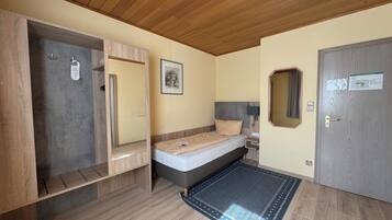 A bedroom with a bed, a bedside table, a mirror, a door, and a wooden ceiling.