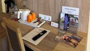 Escritorio de habitación de hotel con espejo, toma de corriente, tetera, cafetera, botella de agua, control remoto y folletos informativos.