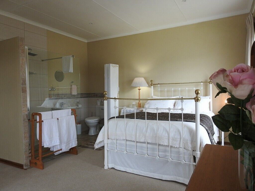 A bedroom with a bed, a bedside table, a lamp, a mirror, a bathroom with a toilet, and a shower.