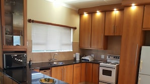 Una cocina con gabinetes de madera, encimera negra, estufa, pileta y microondas.