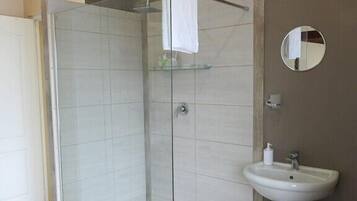 A modern bathroom with a glass shower enclosure, a pedestal sink, and a round mirror.