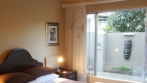 Un dormitorio con cama, mesita de noche, lámpara, ventana con cortinas y vistas al exterior.