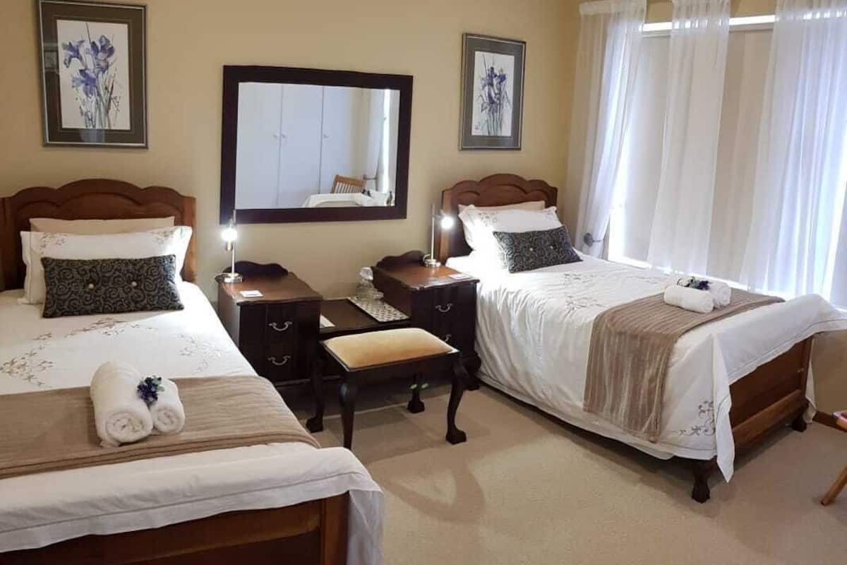 Hotellihuone, jossa on kaksi sänkyä, yöpöytä lampun kanssa, tuoli ja suuri ikkuna, jossa on verhot.