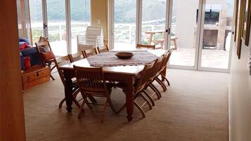 A dining area with a large wooden table and chairs, a buffet setup, and a view through large glass doors.