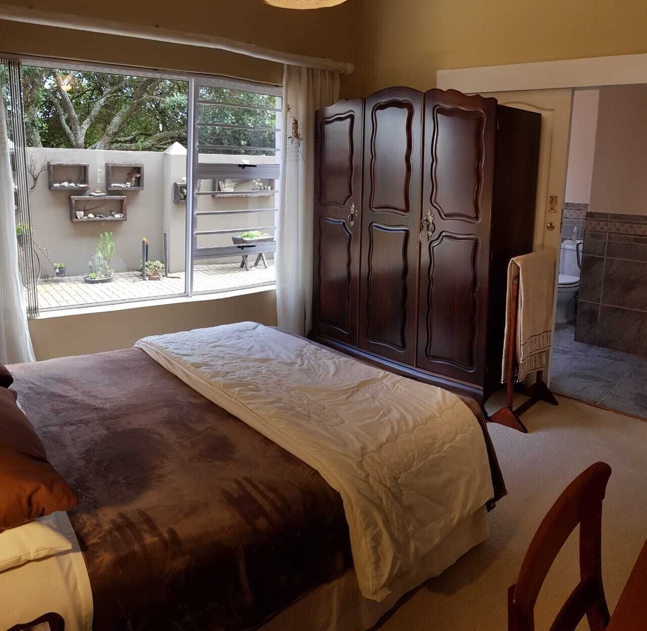 A bedroom with a large bed, a wardrobe, a bathroom, and a view of the outside.