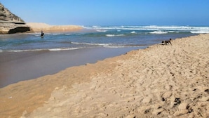 Una playa con un acantilado rocoso, olas y huellas.