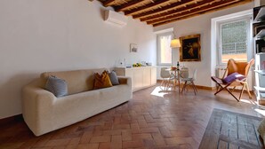 A cozy living room with a wooden ceiling, a sofa, a dining area with chairs, and a view through a window. - Casa Modelli (Rome)