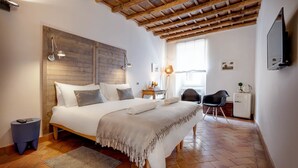 A bedroom with a wooden headboard, a bed with white linens, a desk with a chair, a television, and a window with natural light. - Casa Modelli (Rome)