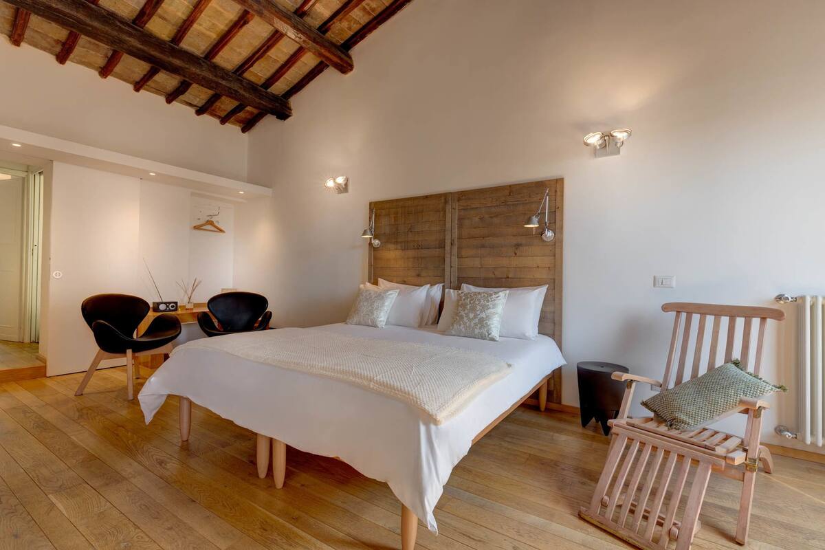 A bedroom with a large bed, wooden headboard, bedside lamps, a chair, and a radiator.
