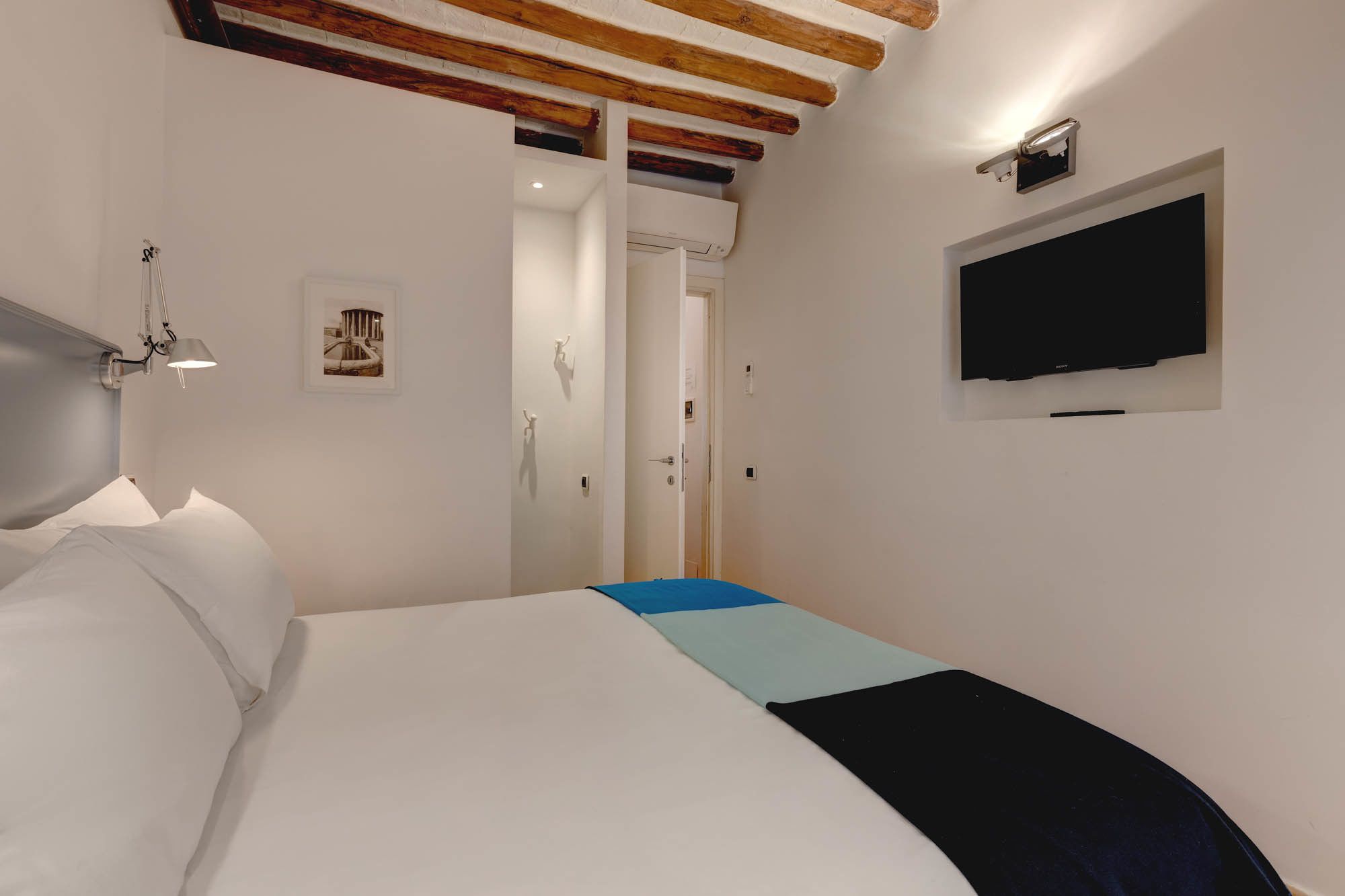 Ein Schlafzimmer mit einem Bett, einem an der Wand montierten Fernseher und einer Tür zu einem anderen Raum.