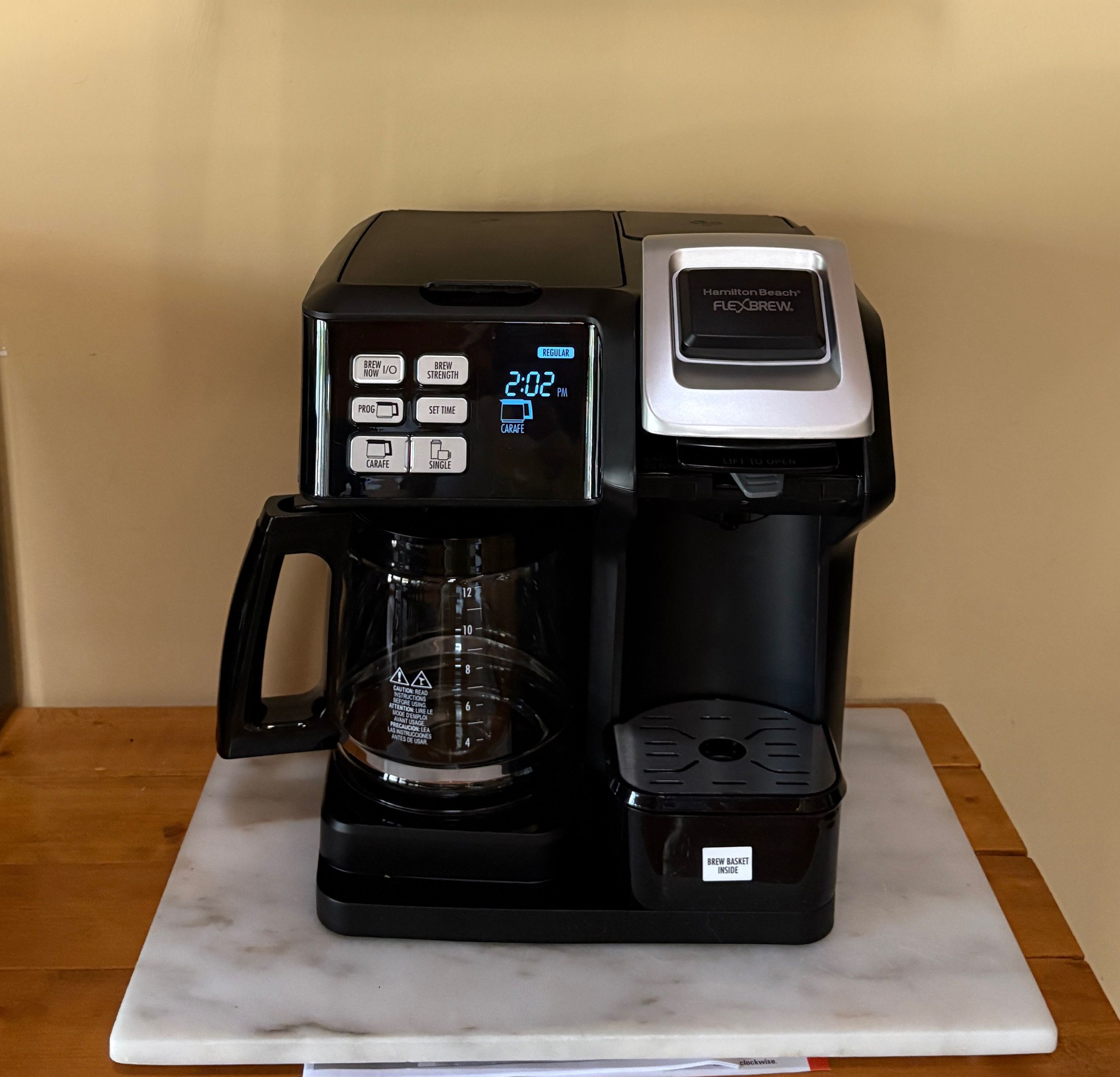 Une machine à café dotée d’un écran numérique, d’une verseuse et d’un bac de récupération, posée sur un comptoir en marbre.