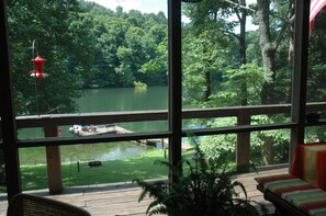 A view from a room with large windows overlooking a lake, a dock, and a grassy area with a red lantern.
