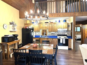 A kitchen with wooden cabinets, a dining table with chairs, a chandelier, and a microwave. - Cabin/Vacation Home In the Woods on Private Lake Close to Louisville, Ky (Elizabeth)