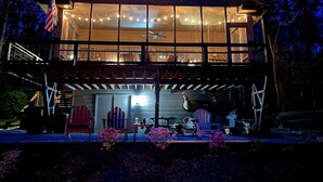 Una cabaña de madera de dos pisos con ventanas amplias, una terraza y luces colgantes.