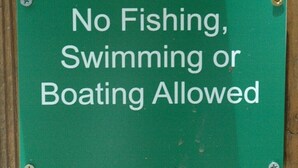 Un letrero verde con texto blanco que indica: 'No se permite la pesca, natación ni navegación'.