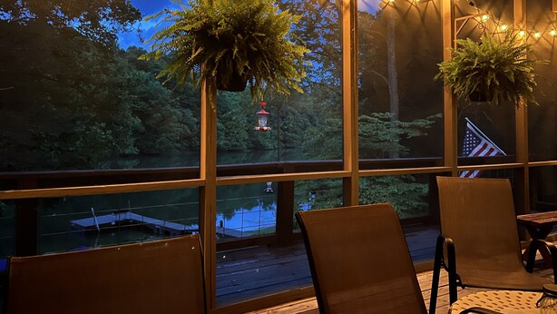 Una habitación con ventanas amplias, terraza de madera y plantas colgantes.