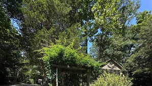 Un jardín con un porche de madera, un banco y una pequeña glorieta.