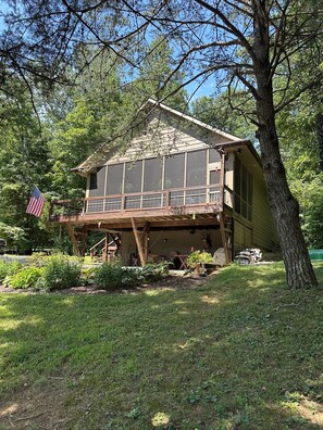 Une cabane en bois à deux étages, dotée d’un balcon et entourée d’arbres, avec un drapeau.