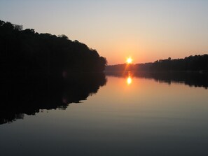 A calm lake at sunrise with trees on the banks.