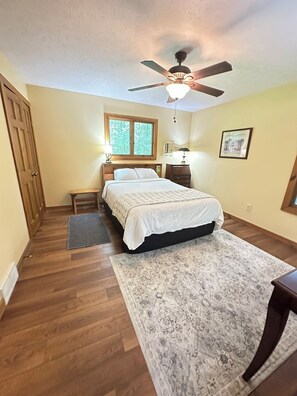 A bedroom with a bed, a ceiling fan, a window, a nightstand, a bedside table, and a rug. - Cabin/Vacation Home In the Woods on Private Lake Close to Louisville, Ky (Elizabeth)