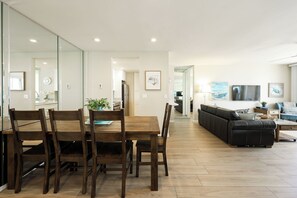 A modern living space with a dining area, a sofa, and a TV. - Premier Beachfront Condo with Breathtaking Ocean Views | 2 Suites (Oceanside)