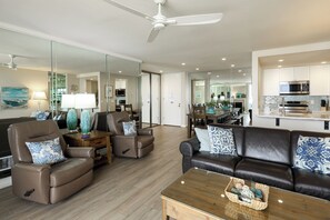 A modern living room with a leather sofa, armchairs, a coffee table, and a dining area with a glass partition. - Premier Beachfront Condo with Breathtaking Ocean Views | 2 Suites (Oceanside)