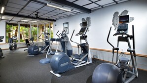 Ein Fitnessraum mit verschiedenen Trainingsgeräten, einem großen Fenster mit Blick auf Grünflächen und einer Decke mit Gittermuster.