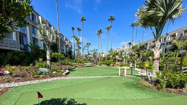 Ein Golfplatz mit Putting Green, umgeben von Palmen und einem Gebäude mit Balkonen.