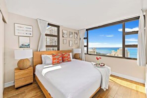 A bedroom with a large window, a bed, a nightstand, and a bedside table.