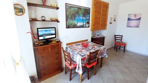A small, cozy room with a wooden desk, a computer, a bed with a quilt, and a dining table with chairs. - La Piaggia (Rio)
