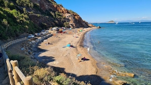 A coastal beach with a rocky cliff, clear blue sea, and a wooden fence along the path. - La Piaggia (Rio)