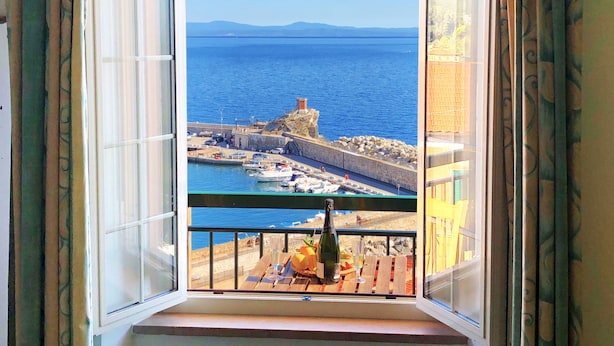 A balcony with a clear view of the sea, a rocky coastline, and a distant mountain range. - Le Maree Fede (Rio)