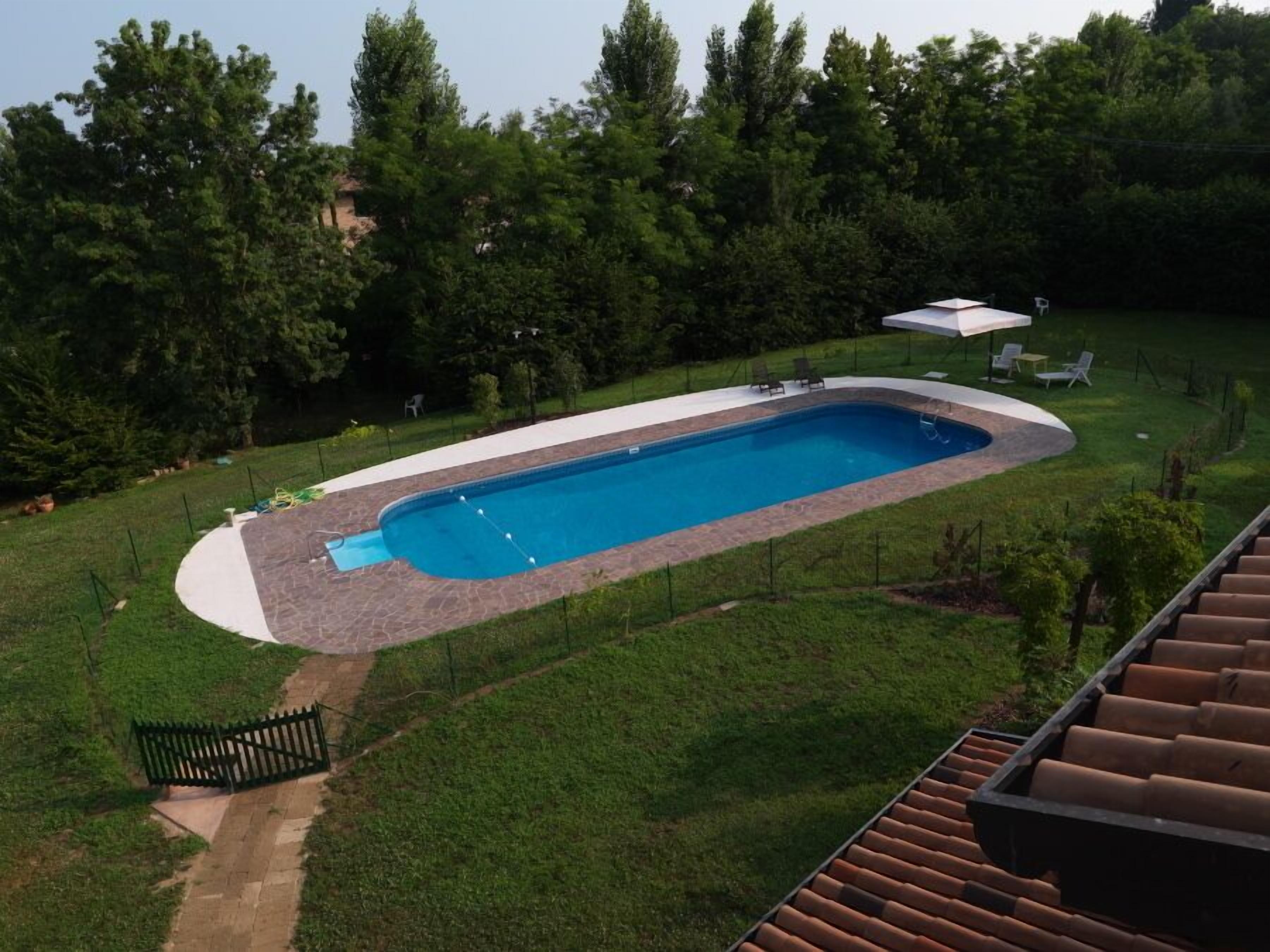 Piscina rectangular con borde de piedra, rodeada por un césped y árboles.