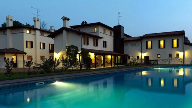 Una casa grande y moderna con piscina, rodeada de césped y árboles bien cuidados.
