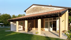 Una casa con porche cubierto, fachada de piedra y una piscina al fondo.