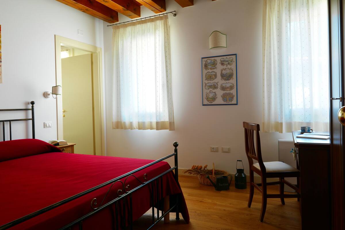 Un dormitorio con cama, una silla, un escritorio y una ventana con cortinas.