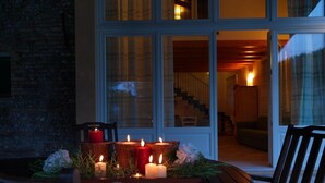 Una mesa redonda de madera con sillas, velas encendidas y una cesta de mimbre con flores.